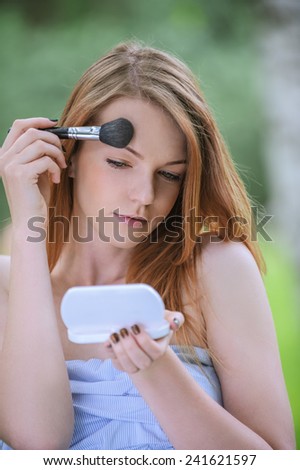 Beautiful young woman with bare shoulders eyes colors and mirror, against green of summer park.