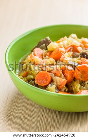 Fries with meat, cabbage and carrots in green plate on wooden table.