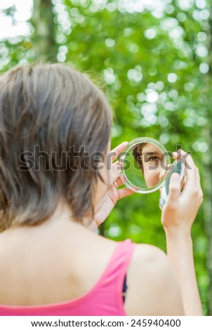 Lovely girl looks in round mirror against summer green park.