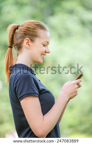 Beautiful smiling young woman profile in dark blouse talking on mobile phone, against green of summer park.