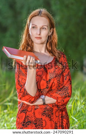 Young beautiful woman glances over working writing-book against evening park.