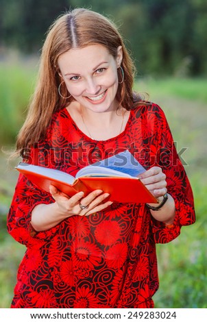 Young beautiful woman glances over working writing-book against evening park.