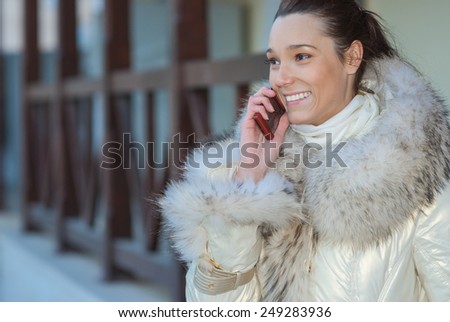 Young smiling beautiful woman in white coat with fur collar talking on mobile phone.