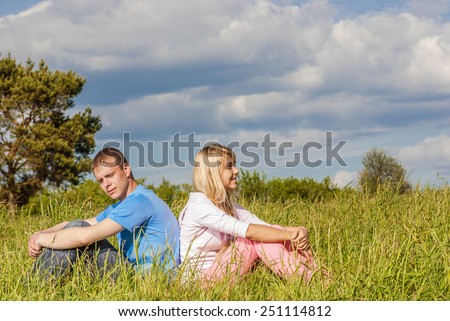 outdoor portrait of young couple sitiing on green grass back to back