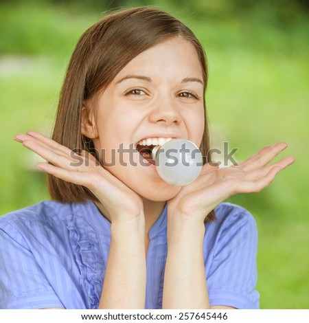 Close-up portrait of young funny amazed woman holding light bulb in teeth.