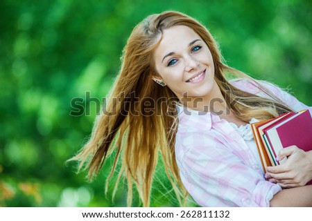 Portrait of beautiful smiling young woman with books, against green of summer park.