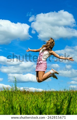 Beautiful young woman close-up jumping, against green of summer park and blue sky.