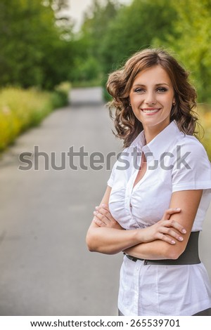 Portrait of beautiful young brunette woman wearing white blouse at summer green park.