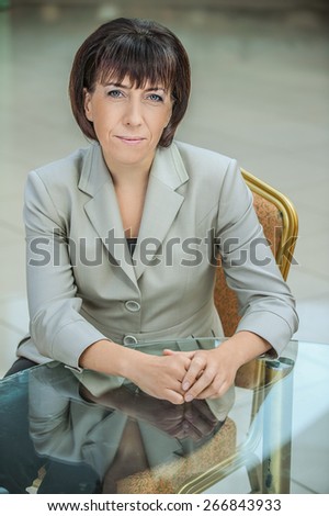 Beautiful businesswoman in bright suit sitting at glass table.
