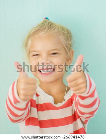 Little cheerful girl lifts thumb upwards, on green background.