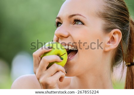 portrait young charming blonde woman biting green apple background summer park
