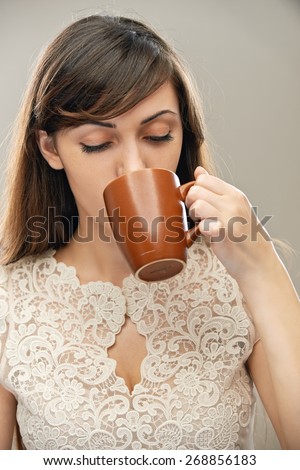 young beautiful dark-haired woman drinking tea from mug, on gray background