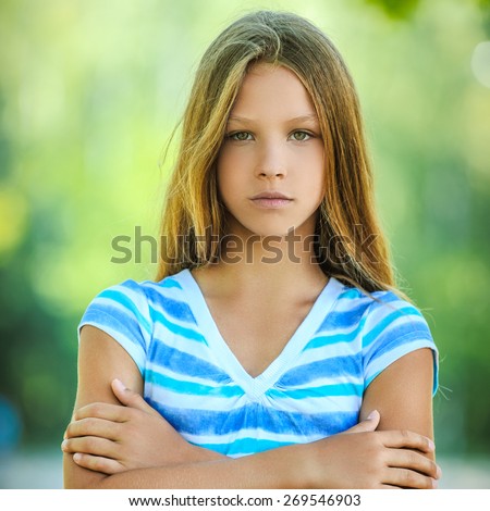 Beautiful sad teenage girl in blue blouse, against green of summer park.