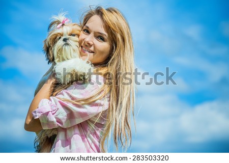 Portrait of beautiful smiling young woman with small dog, against blue sky.
