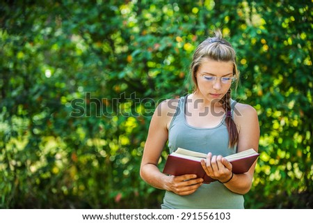 Beautiful young woman reads book, against green of summer park.
