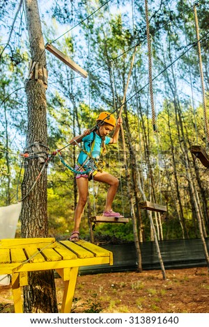 Girl climbing in adventure park is a place which can contain a wide variety of elements, such as rope climbing exercises, obstacle courses and zip-lines.