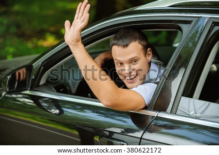 Portrait of young attractive handsome brunette man driving car and greeting somebody with hand.