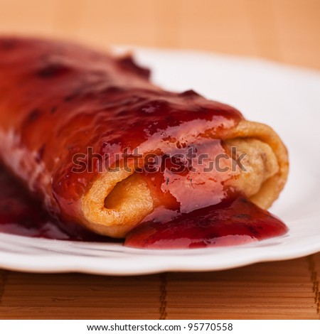 on white plate pancake stuffed with folded in roll filled jam against a bamboo napkin