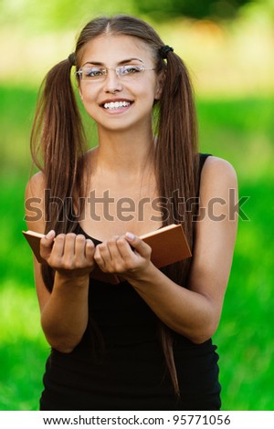 Portrait of young attractive smiling woman wearing black blouse and eyeglasses standing at summer green park.