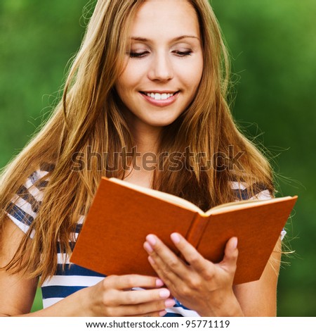 fun, young and charming woman with long hair, holding an open book, read against the background summer green park
