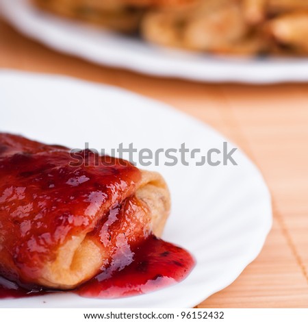 Close-up pancake with jam on saucer next to full meal of pancakes rolled up on bamboo table cloth rolls
