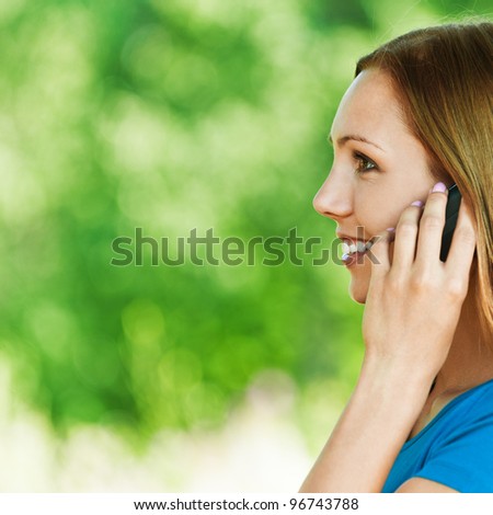 young, attractive woman in profile, said by cell phone, smiling background summer green park