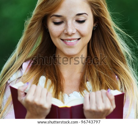 close-up of long-haired, cheerful woman is reading good book on background of summer park