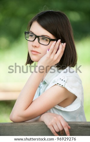 Portrait of young sad brunette woman wearing glasses at summer green park