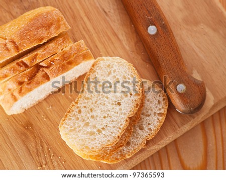 Close-up sliced ??bread (long loaf) on cutting wooden board, knife