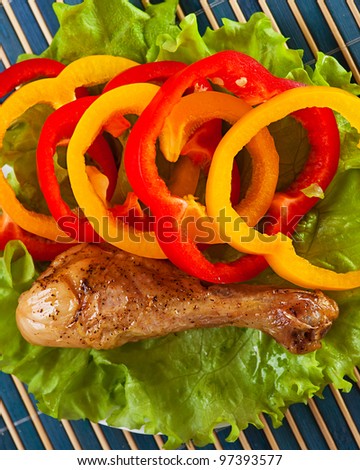 on blue bamboo napkin with plate of food: Lettuce, they cut slices sweet Bulgarian pepper and fried, very tasty-looking chicken drumstick-top view