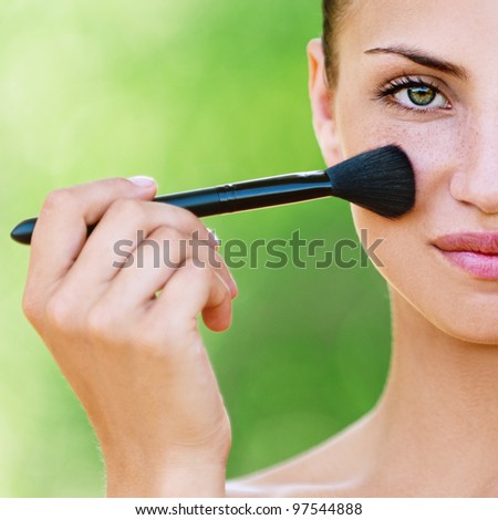 portrait half face of beautiful dark-haired sexy girls with makeup brush in hand on green background