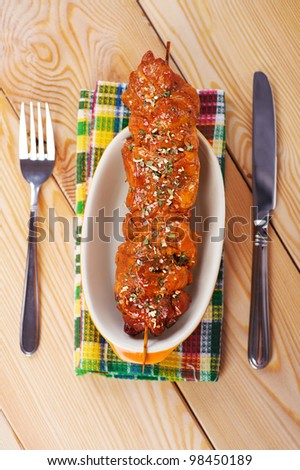 against the background of the wooden kitchen table on checkered cloth, mouth-watering meat kebab (pork, beef, lamb, chicken) on skewer in large bowl, knife, fork