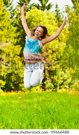funny, beautiful, young woman jumps up on the background of green grass and forest