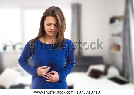 Young woman suffering stomach ache pressing abdomen because of burn acid as digestive illness problem concept on indoor room background