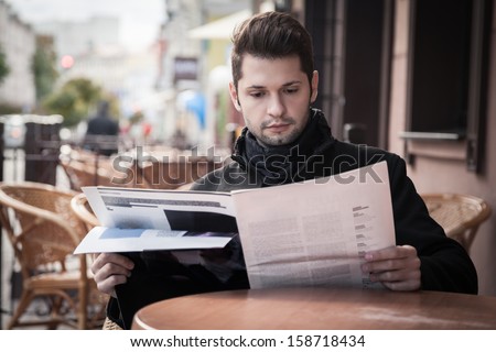 Handsome Young Man Reading A Magazine In A Cafe On The Street