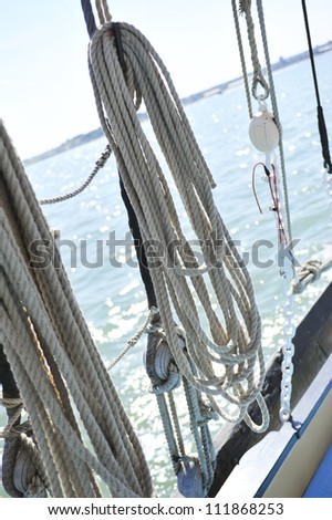 coiled rope hanging from the side of a ship rigging with sea and coastline in the distance