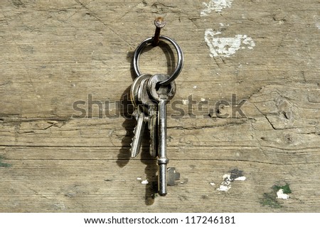 a set of three keys on ring hanging on rusty nail on wood