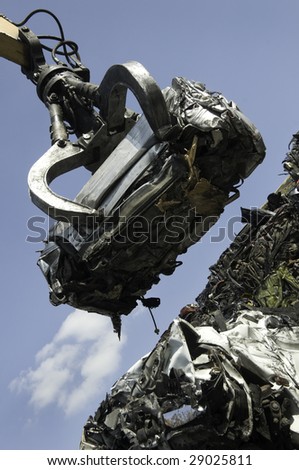 A scrap car being lifted by grab crane on to a pile of other scrapped cars.
