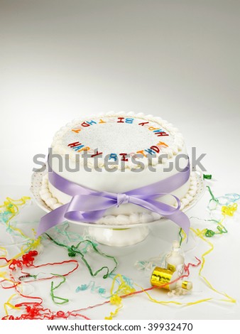 A white birthday cake on cake stand with party streamers