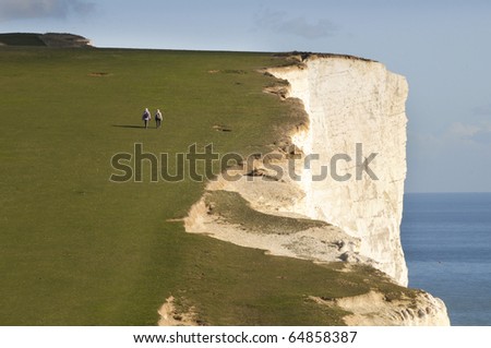 Seen from the rear  and at a far distance two walkers on the South Downs coastal cliff path in Sussex