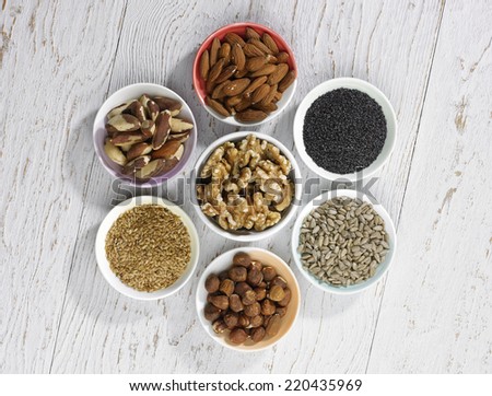 a selection of four different types of nuts and three types of seeds in bowels on a white wooden background