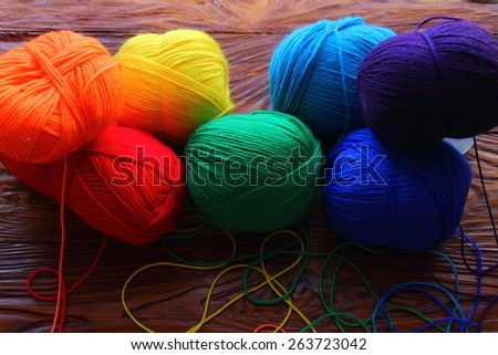 on a wooden board are colored balls of threads for knitting