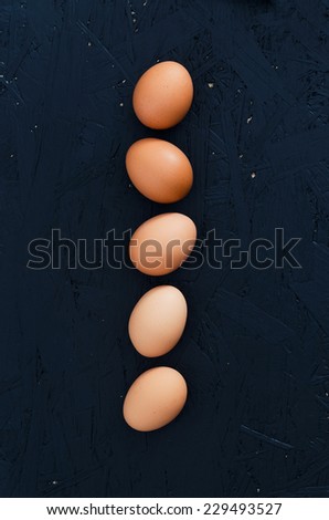 Eggs arranged in straight line over dark background. Overhead view