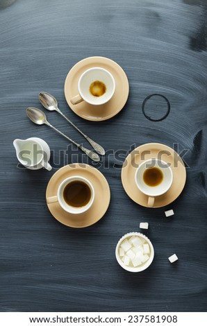 Coffee cups, milk jar and spoons  over chalk textured table, above view