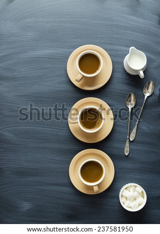 Coffee cups, spoons and milk jar over chalk textured table, above view