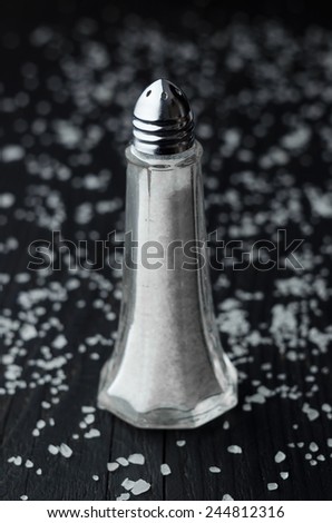 Close up of salt shaker over black wooden table with salt all over it