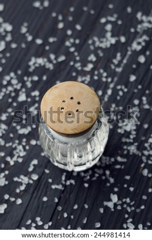Rustic salt shaker over black wooden table with salt all over it