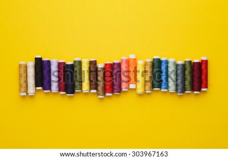Colorful thread spools in a row over bright yellow background, above view