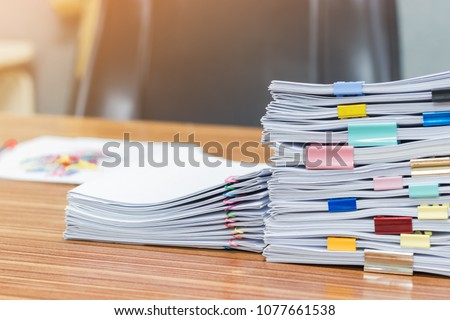 Stack of student\'s homework that assigned to students to be completed outside class on teacher\'s desk separated by colored paper clips. Document stacks arranged by various colored paper clips on desk.