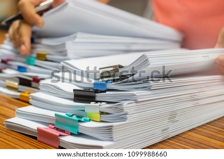 Teacher hand holds pen for checking student's homework assignment on table office. Paper documents stacked in archive with paperclip. Report papers stacks. Business and education concept.